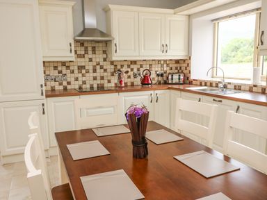 A kitchen with white cabinets a wooden dining table with placemats and a vase of flowers at Dromstabla in Glencar