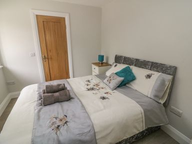 A bedroom with a bed with floral bedding and towels beside a wooden door and a nightstand with a blue lamp at Dromstabla in Glencar