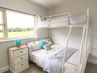 A bedroom with a bunk bed a small bedside table with a blue lamp and a window showing greenery at Dromstabla in Glencar