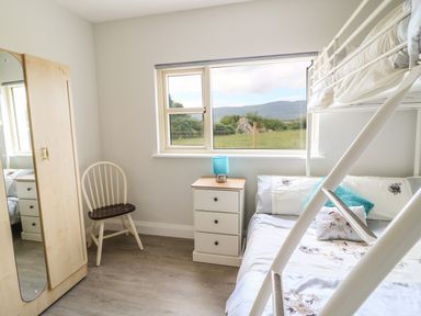 A bedroom with a bunk bed a white chair a three drawer nightstand with a blue lamp and a wardrobe with a mirror at Dromstabla in Glencar