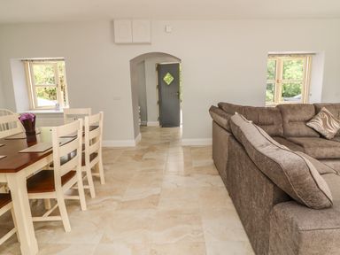 A dining area with table and chairs next to a living area with a large sectional sofa and windows at Dromstabla in Glencar