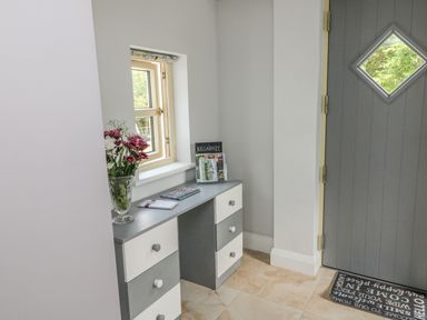 An entryway with a gray door with a diamond window a small table with drawers flowers books and brochures on it at Dromstabla in Glencar