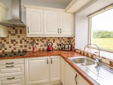 A kitchen with white cabinets wooden countertops a stainless steel sink a window and appliances at Dromstabla in Glencar