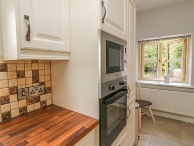 A kitchen with wood countertop tiles on the wall built in oven microwave and a window with a chair below it at Dromstabla in Glencar