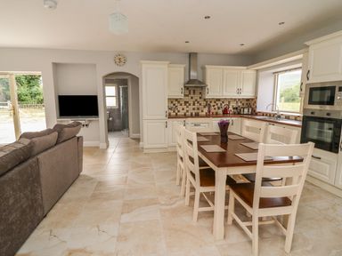 An open kitchen and dining area with white cabinets a wooden dining table with six chairs and a gray sofa at Dromstabla in Glencar