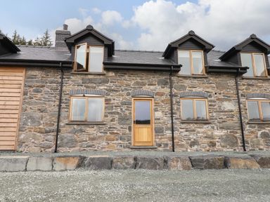 Stone exterior wall with wooden door and windows under a cloudy sky at Llety Dewi in Lake Vyrnwy