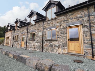 Stone house exterior with wooden doors and windows and gravel ground at Llety Dewi in Lake Vyrnwy