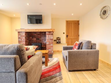 A living room with two grey sofas a wooden coffee table a brick fireplace with a mounted TV and a wall clock at Llety Dewi in Lake Vyrnwy