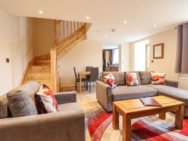 A living room with grey sofas, a wooden coffee table, a red and grey rug, and a staircase at Llety Dewi in Lake Vyrnwy