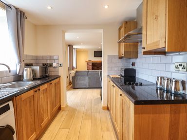 A kitchen with wooden cabinets countertop appliances and a view into a living room with a sofa at Llety Dewi in Lake Vyrnwy