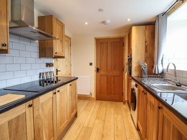 A kitchen with wooden cabinets a stove a sink and a door at Llety Dewi in Lake Vyrnwy