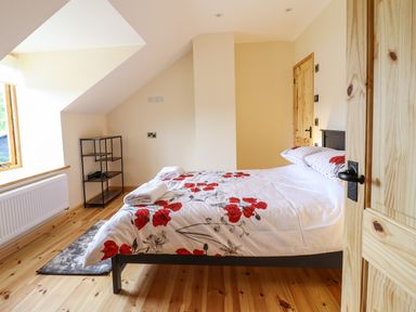 A bedroom with a bed with floral bedding a small shelving unit and a window at Llety Dewi in Lake Vyrnwy