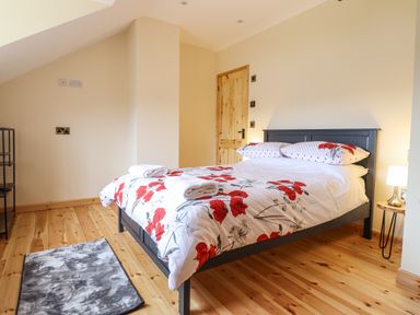 A bedroom with a bed with floral bedding two rolled towels a small lamp on a wooden side table and a grey rug on the wooden floor at Llety Dewi in Lake Vyrnwy