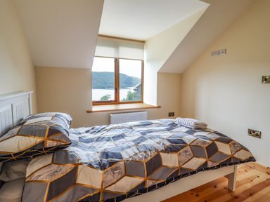 A bedroom with a bed next to a window showing a view of a lake and hills at Llety Dewi in Lake Vyrnwy