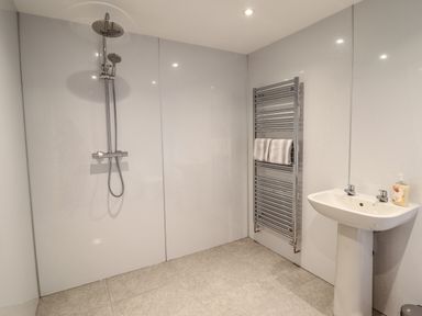 A bathroom with a wall-mounted shower, a towel radiator with towels, and a pedestal sink with soap at Llety Dewi in Lake Vyrnwy