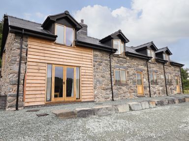 The exterior of a stone and wood house with multiple windows and wooden doors at Old Cart House in Llanwddyn