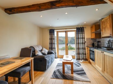 A living area with a gray sofa wooden dining table chairs and a kitchen with wooden cabinets and appliances at Old Cart House in Llanwddyn