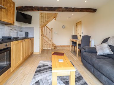 A kitchen and living area with wooden cabinets a grey sofa a wooden table with two chairs and a staircase at Old Cart House in Llanwddyn