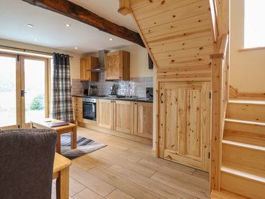 A kitchen with wooden cabinets a stove and sink next to wooden stairs with storage underneath at Old Cart House in Llanwddyn