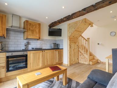 A kitchen area with wooden cabinets a built-in oven a microwave and a wooden staircase in a living space at Old Cart House in Llanwddyn