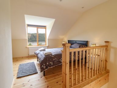 A bedroom with a bed and two lamps near a window overlooking a lake at Old Cart House in Llanwddyn