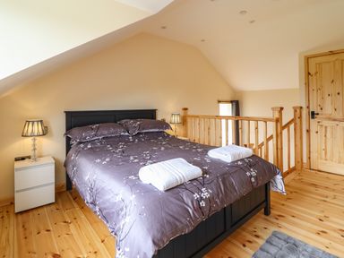 A bedroom with a double bed with floral bedding and towels on the bed beside a wooden railing and a wooden door at Old Cart House in Llanwddyn
