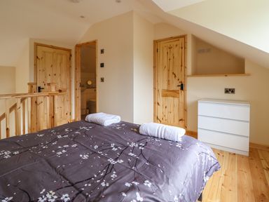 A bedroom with a bed covered in dark floral bedding two rolled white towels on the bed wooden doors and a white chest of drawers at Old Cart House in Llanwddyn