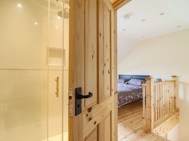 A bedroom with a bed and wooden railing viewed through an open door next to a shower at Old Cart House in Llanwddyn