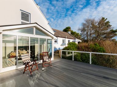 An outdoor deck with two wooden chairs and a bottle of wine outside a house with glass windows at The Schooner in Goleen County Cork