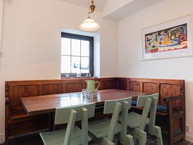 A dining area with a wooden table green chairs a wooden bench under a window and a colorful framed artwork on the wall at The Schooner in Goleen County Cork