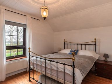 A bedroom with a metal bed frame two bedside tables with lamps and a window with curtains at The Schooner in Goleen County Cork