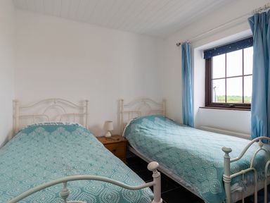 A bedroom with two single beds with blue patterned bedspreads a wooden nightstand with a lamp and a window with blue curtains at The Schooner in Goleen County Cork