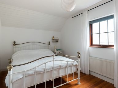 A bedroom with a metal bed frame white bedding a window with curtains and a small bedside table at The Schooner in Goleen County Cork