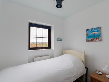 A bedroom with a bed covered in white bedding next to a window and a wooden nightstand at The Schooner in Goleen County Cork