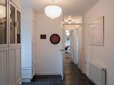 A hallway with a dartboard on the wall and white cabinets with an open door showing a room with flowers at The Schooner in Goleen County Cork