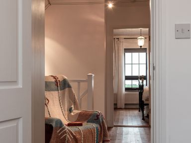 A chair with a patterned blanket and a book on it near a doorway leading to a bedroom with a black bed frame and a window at The Schooner in Goleen County Cork