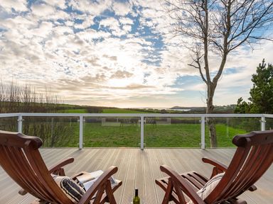 Two wooden chairs with cushions on a balcony overlooking green fields and a distant coastline at The Schooner in Goleen County Cork