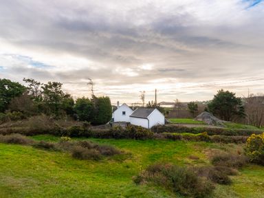 A white house surrounded by trees and green grass with a cloudy sky at The Schooner in Goleen County Cork