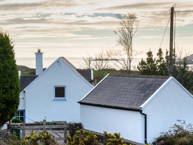 A view of white houses with gray roofs near the coast with a telephone pole and trees at The Schooner in Goleen County Cork