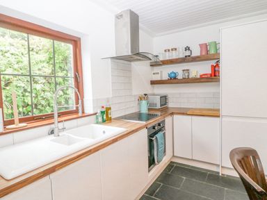A kitchen with a white sink and faucet wooden countertops an oven stove and microwave with shelves holding jars and teapots at The Schooner in Goleen County Cork