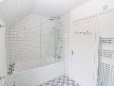 A bathroom with a bathtub shower combo white tiled walls patterned floor tiles and a towel radiator at The Schooner in Goleen County Cork