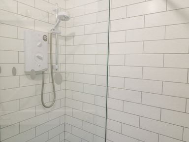 A corner shower with white tiled walls showerhead and an electric shower unit at The Schooner in Goleen County Cork