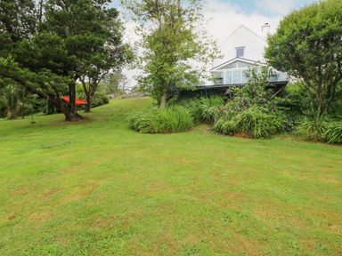A grassy yard with trees and bushes and a white house with a glass porch at The Schooner in Goleen County Cork