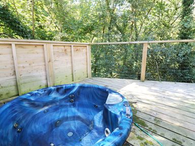 An outdoor wooden deck with a blue hot tub surrounded by trees at 6 Streamside in Lanreath