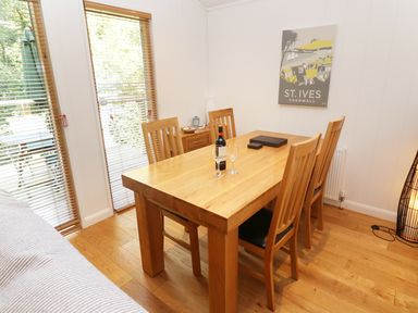 A dining room with a wooden table and chairs a bottle of wine and glasses on the table and a St Ives Cornwall poster on the wall at 6 Streamside in Lanreath
