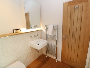 A bathroom with a wall-mounted sink and faucet a towel rack with a white towel and a wooden door at 6 Streamside in Lanreath