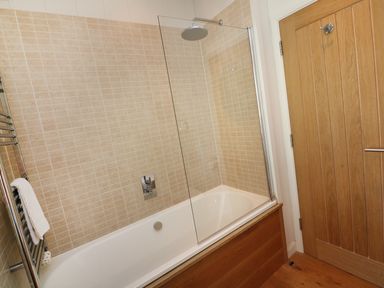 A bathroom with a bathtub shower combination with beige tiled walls and a wooden door at 6 Streamside in Lanreath