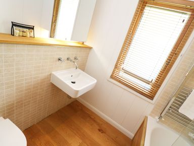 A bathroom with a wall-mounted sink, wooden floor, window blinds, and a bathtub at 6 Streamside Lanreath