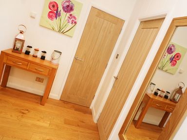 A hallway with two wooden doors a wooden table with decorative items and a floral painting above the table at 6 Streamside in Lanreath