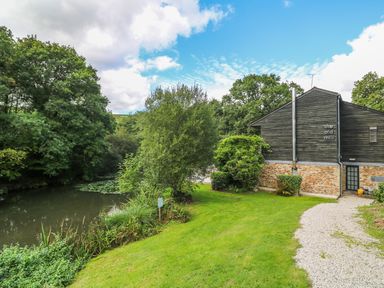 A pond and green trees next to a building with stone and wood exterior at 6 Streamside in Lanreath